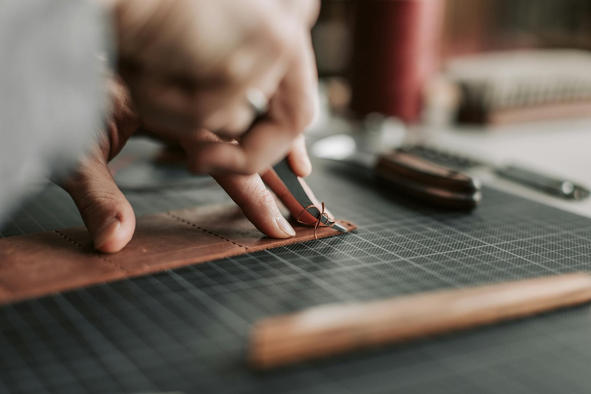 Nahaufnahme eines Arbeiters beim Zuschneiden von Leder auf einem Arbeitstisch. Das Bild vermittelt Handwerkskunst und Innovation, während im Text die Herstellung individueller und innovativer Produkte hervorgehoben wird.